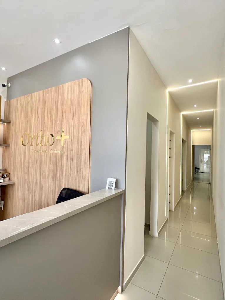 Recepção da Orthomais, com a logomarca em dourado sobre o painel de madeira e o corredor de atendimento ao fundo.